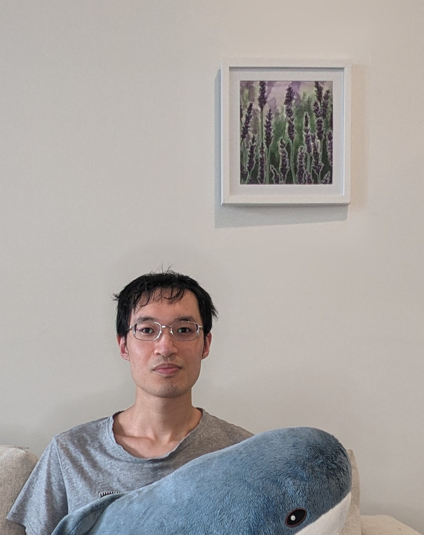 Chris holding a blåhaj, with a painting of lavender in the background